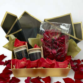 Gift box with red rose petals, candles, and Godiva chocolates