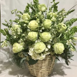 Tall basket arrangement of pale green and white flowers with roses and hydrangeas.