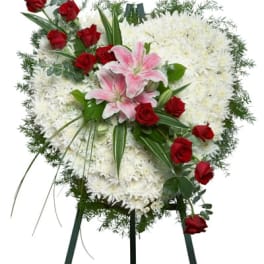 Heart-shaped white floral standing spray with pink lilies and red roses on an easel