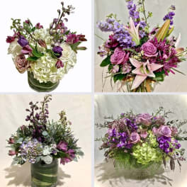 Four purple and white mixed flower arrangements in clear glass vases with roses, hydrangeas and accent blooms.
