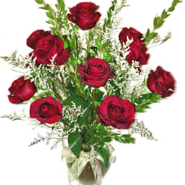 Tall arrangement of red roses with white filler flowers in a clear glass vase tied with a ribbon.