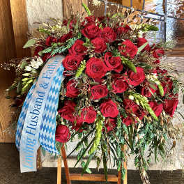 Tall standing spray of red roses with cascading greenery and a memorial ribbon on an easel.