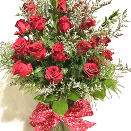 Tall arrangement of red roses with white filler flowers in a clear glass vase with a red bow.