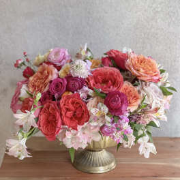 Mixed pink and coral flowers arranged in a gold pedestal vase