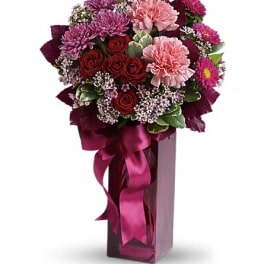 Bouquet of pink and red flowers in a tall glass vase with a ribbon