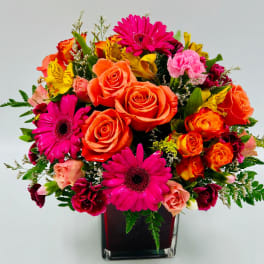Bright mixed bouquet of roses, gerbera daisies, and carnations in a square vase
