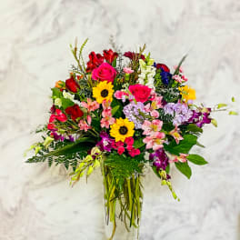 Mixed bouquet of roses, sunflowers, and orchids in a glass vase