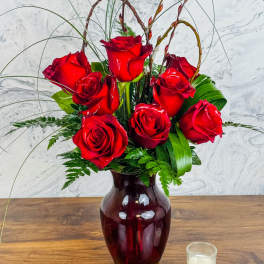 Red roses arranged in a burgundy vase with tall decorative stems