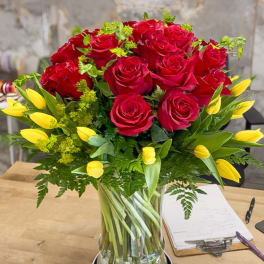 Red roses and yellow tulips arranged in a clear glass vase