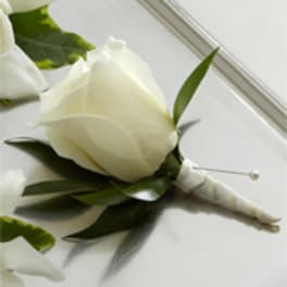 White rose boutonniere with wrapped stem and pearl pin on a white surface