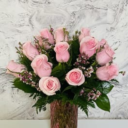 Pink roses arranged in a tall pink glass vase with a small candle nearby