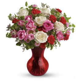 Red, pink, and white mixed bouquet of roses and carnations in a red glass vase
