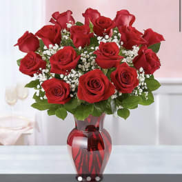 Red roses arranged in a red glass vase with white filler flowers