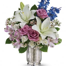 Bouquet of white lilies, pink roses, and blue flowers in a silver vase