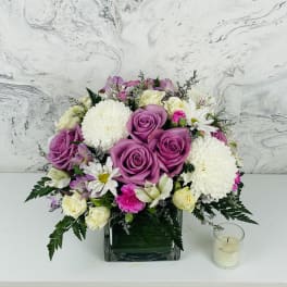 Pink and white rose bouquet in a square glass vase with a small candle beside it.