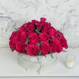 Hot pink roses arranged in a round white box with a ribbon bow