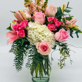 Pink roses and lilies arranged in a glass vase with white hydrangea