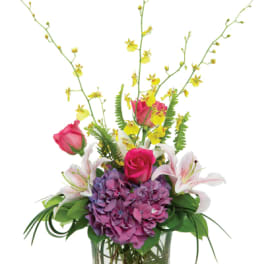 Tall arrangement with pink roses, lilies, purple hydrangea and yellow orchids in a glass vase with stones