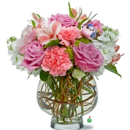 Short round arrangement of pink roses, carnations, and white blooms in a clear glass bowl vase