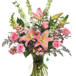 Tall arrangement of pink lilies and roses with white flowers in a clear glass vase