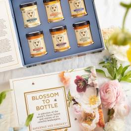 Gift box with six honey jars beside floral packaging