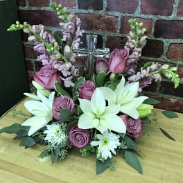 Pink roses and white lilies arranged around a clear glass cross
