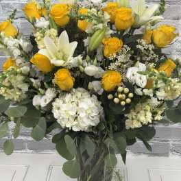 Yellow roses and white lilies arranged in a clear glass vase