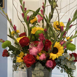 Tall mixed bouquet in a metal vase with sunflowers, red roses, and pink blooms