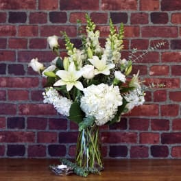 Tall arrangement of white lilies, roses, and hydrangeas in a clear glass vase