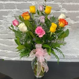 Bouquet of multicolored roses in a glass vase with a pink ribbon