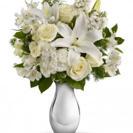 Arrangement of white lilies, roses, carnations, and alstroemeria in a shiny silver vase.