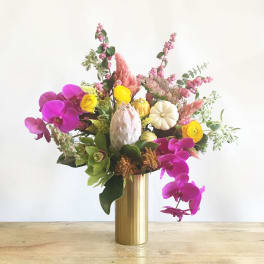 Mixed floral arrangement in a gold vase with pink orchids and yellow blooms