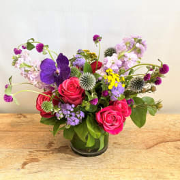 Mixed bouquet of pink roses, purple orchids, and small wildflowers in a glass vase