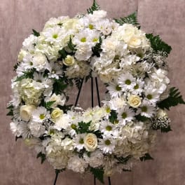 Large white and cream floral wreath with roses, daisies, and carnations on a stand
