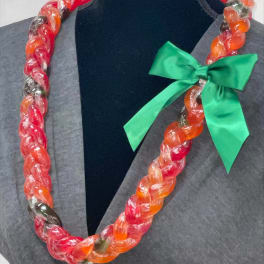 Braided candy lei in red and orange hues with a green satin bow on a display bust.