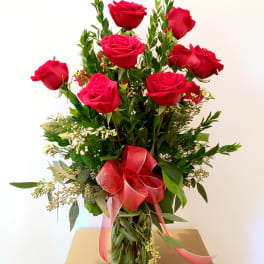 Red roses arranged in a clear glass vase with a pink ribbon