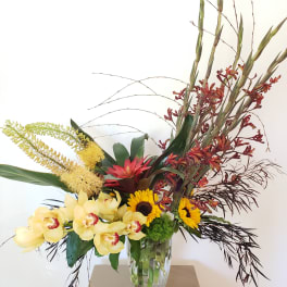 Tropical flower arrangement in a clear glass vase with orchids and sunflowers