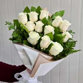 Bouquet of white roses wrapped in white paper with green foliage