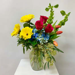 Bouquet of yellow daisies, red roses, blue hydrangea, and orange tulips in a glass vase