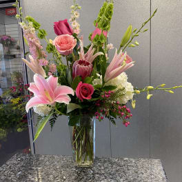 Tall mixed bouquet of pink lilies, roses, and protea in a glass vase