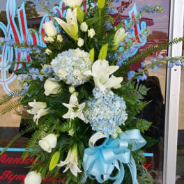 Standing floral spray with white lilies, blue hydrangeas, and a blue ribbon