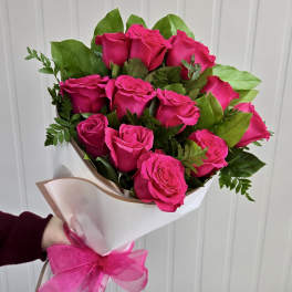 Bouquet of bright pink roses wrapped in white paper with a pink ribbon