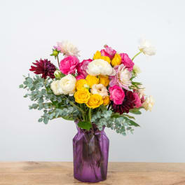 Mixed bouquet of pink, yellow, white, and burgundy flowers in a purple vase