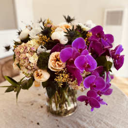 Bouquet of purple orchids, peach roses, and pale hydrangeas in a glass vase