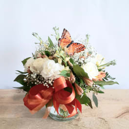 Mixed white and peach bouquet in a glass vase with a red ribbon and butterfly topper