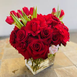 Red roses and pink tulips arranged in a clear square vase