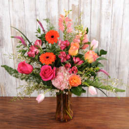 Tall mixed arrangement of pink and orange flowers in an amber glass vase