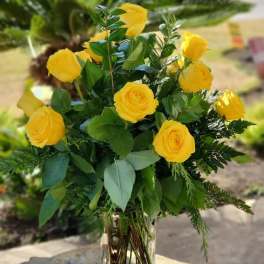 Tall arrangement of yellow roses with lush greenery in a clear glass vase