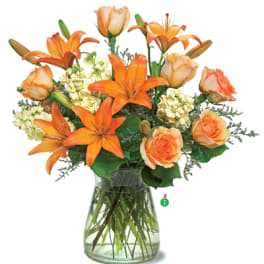 Orange lilies and peach roses with cream flowers arranged in a clear glass vase