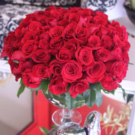 Large dome of red roses arranged in a clear glass pedestal vase